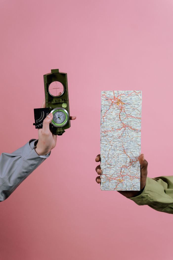 Hands holding a compass and map against a pink backdrop, symbolizing travel planning.